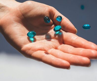Hand holding several translucent blue liquid gel capsules falling into a palm. Supplement evaluation.