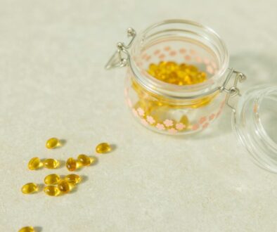 Yellow liquid softgel capsules spilled on a neutral stone countertop next to an open decorative glass jar.