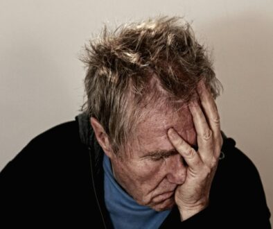 A man with messy hair holding his hand to his forehead and face with a stressed or tired expression against a neutral background. Increase mental clarity after 45.